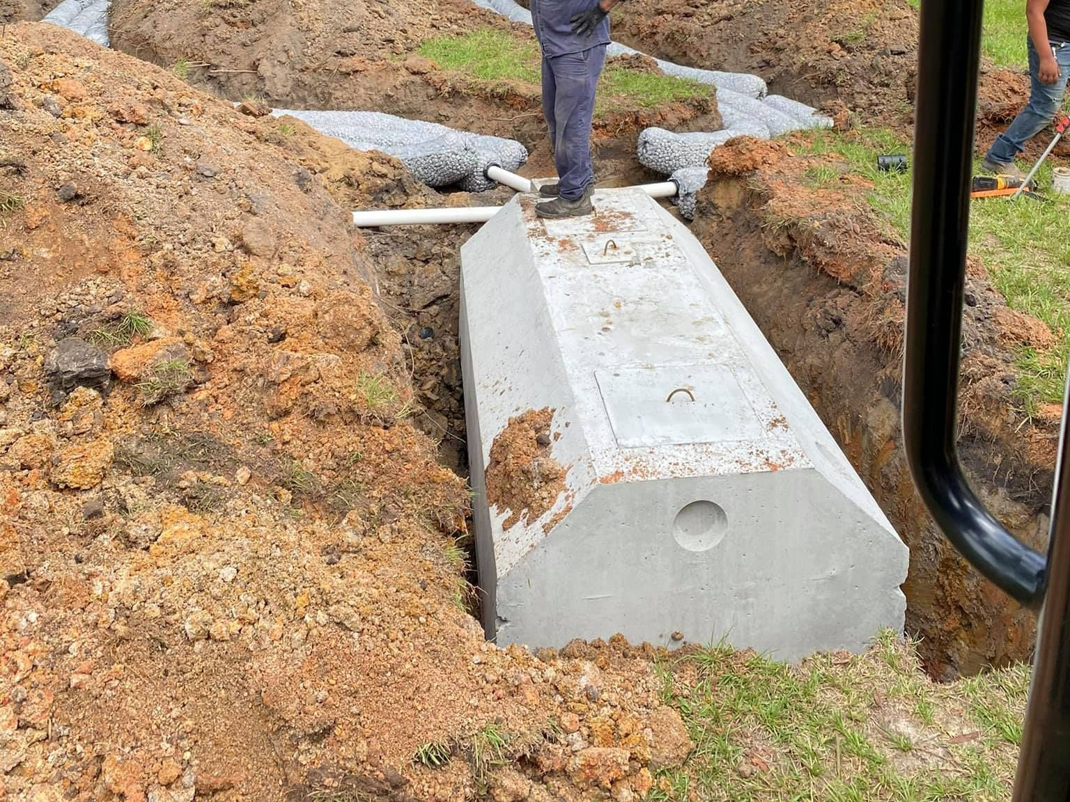 A large concrete septic tank in a dirt trench, for underground utility installation, with a person standing on it in Lumberton, NC.