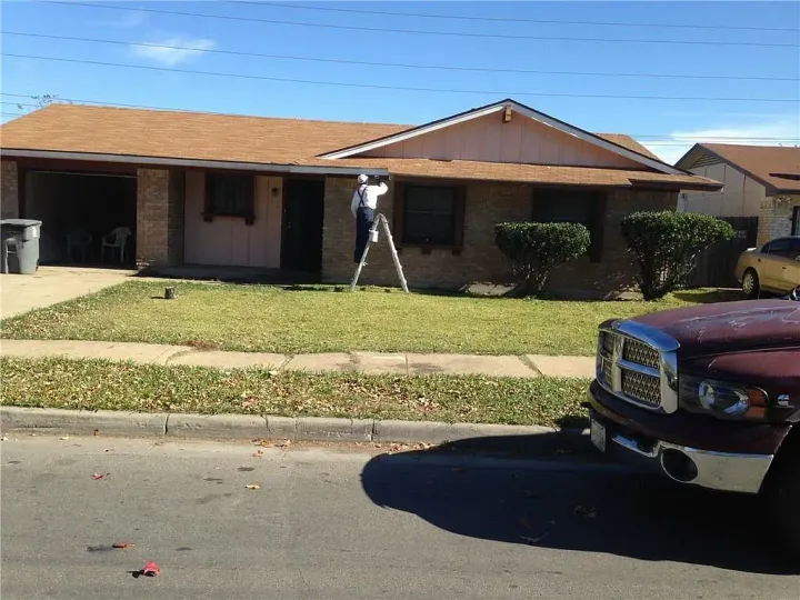 Single-story suburban house with a person in the yard and a red pickup truck parked at the curb.