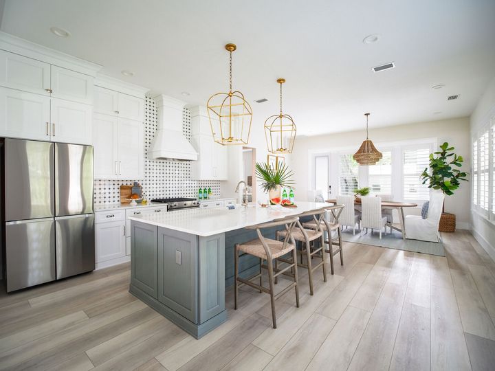 Bright modern kitchen with white cabinets, gray island, stainless fridge, and barstools