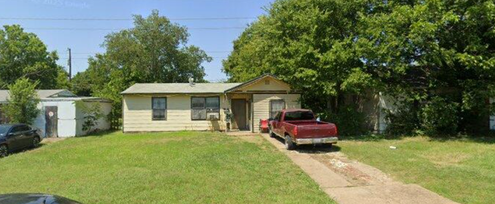 Small beige house with a red pickup truck parked in the driveway and a green lawn in front