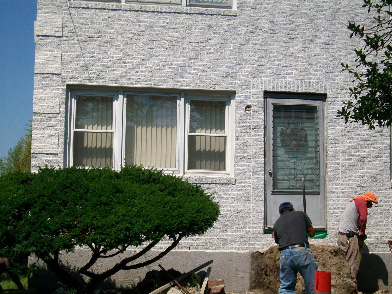 Two men are working in front of a white brick house