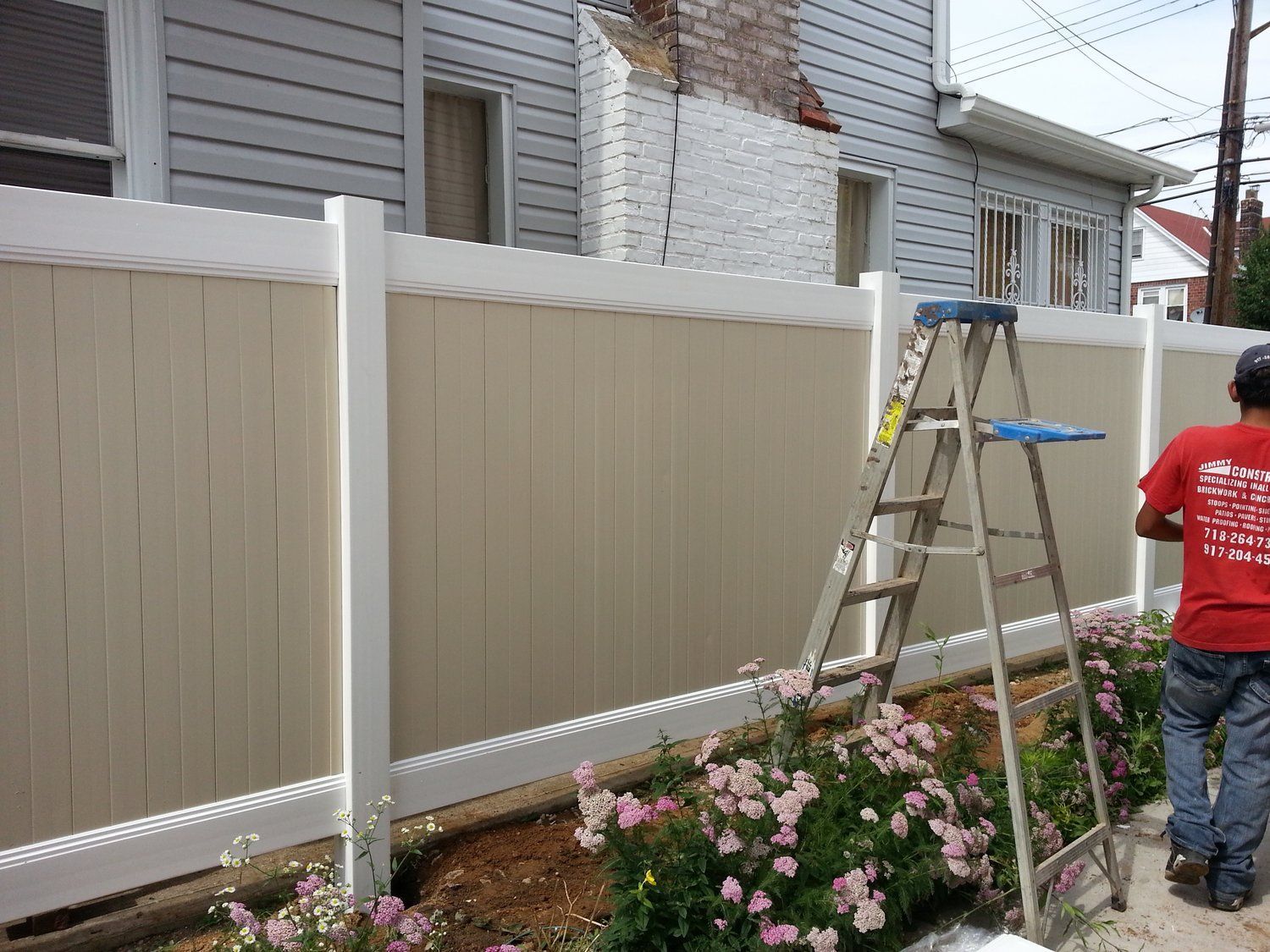 A man in a red shirt is painting a fence
