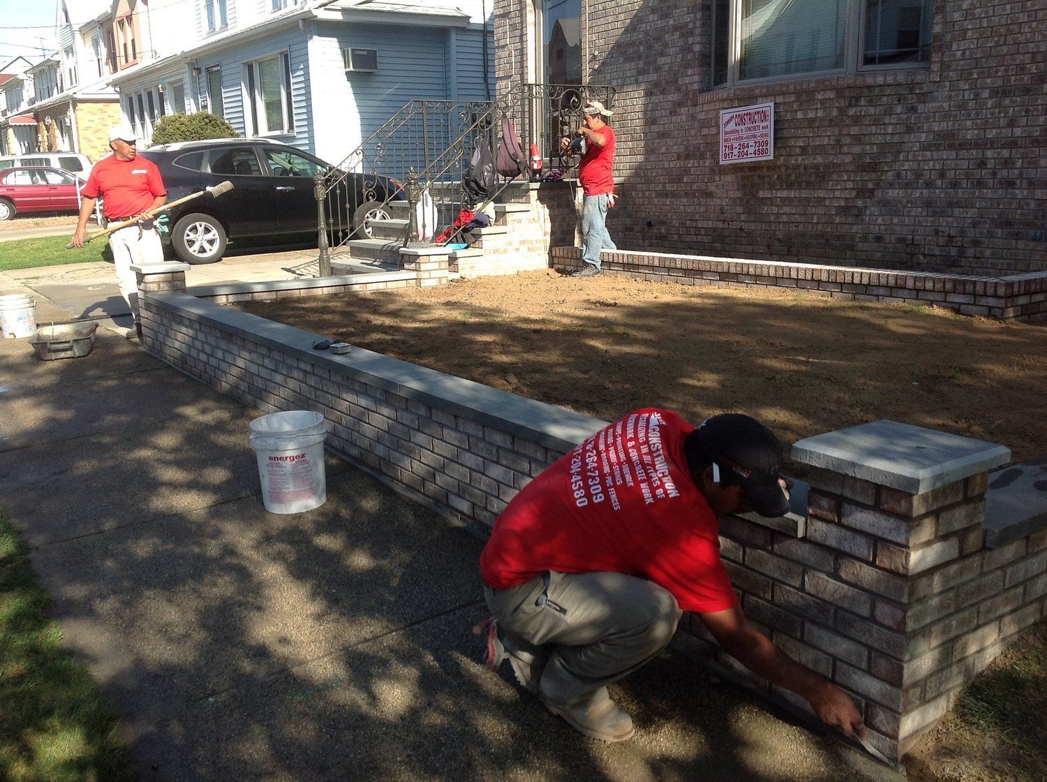 A man in a red shirt is working on a brick wall.