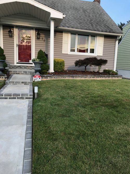 A house with a lush green lawn and a concrete walkway leading to it.