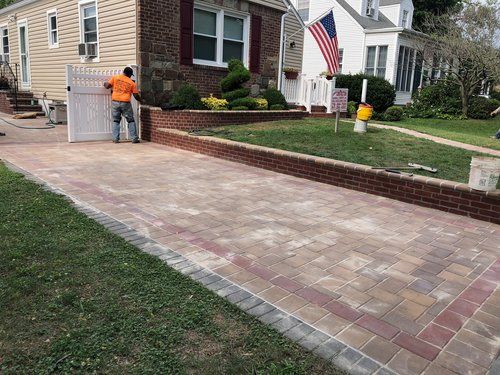A man is standing on a brick driveway in front of a house.