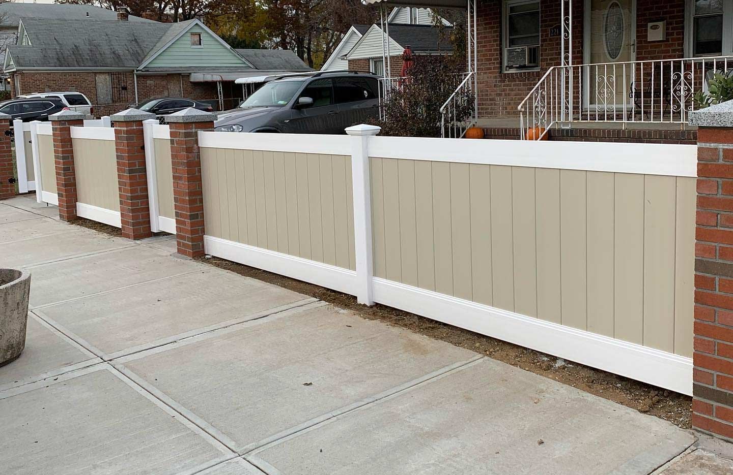 A tan and white fence surrounds a brick house
