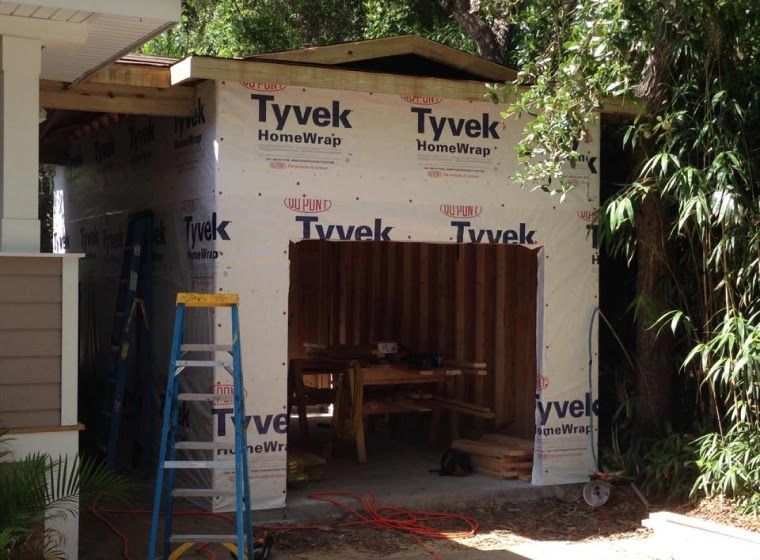 Garage under construction, wrapped with Tyvek. Doorway open, ladder and tools present.