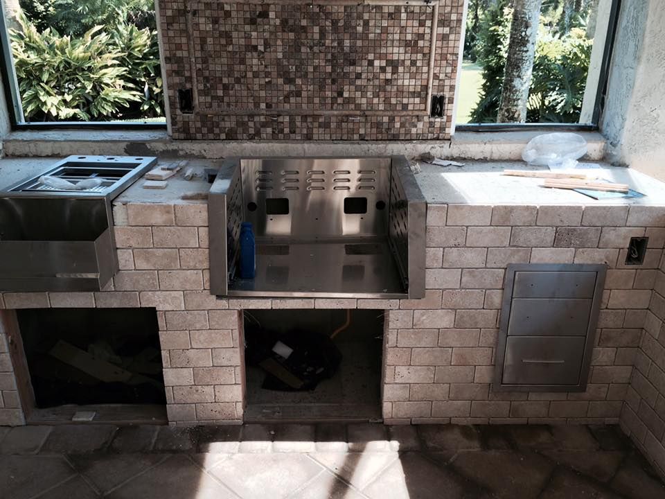 Outdoor kitchen construction: stainless steel grill, sink, and storage compartments set into a brick facade.