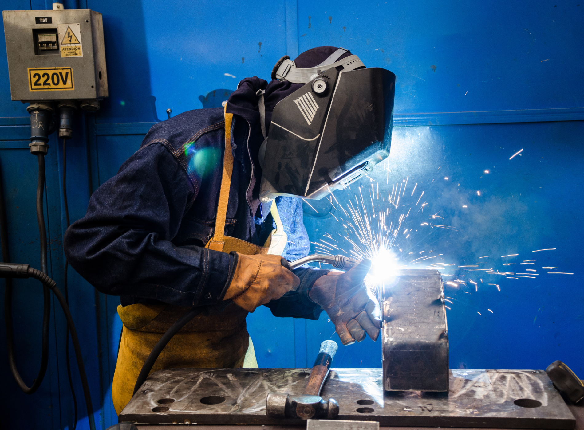 A man wearing a welding mask is welding a piece of metal.