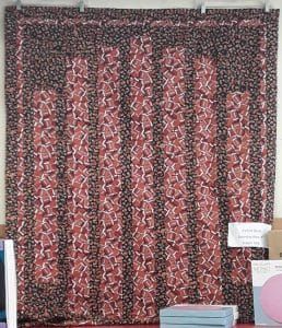 A red and black quilt is hanging on a wall.