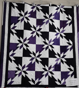 A purple and black quilt is hanging on a wall