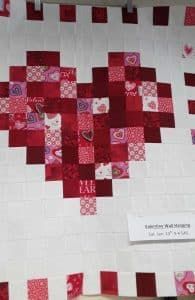 A quilt in the shape of a heart made of red and pink squares.