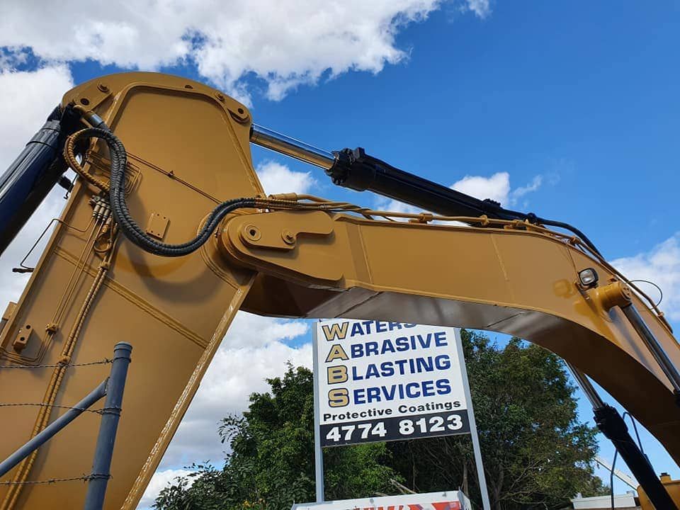 A Large Yellow Excavator With a Sign — Waters Abrasive Blasting Services In Cairns, QLD