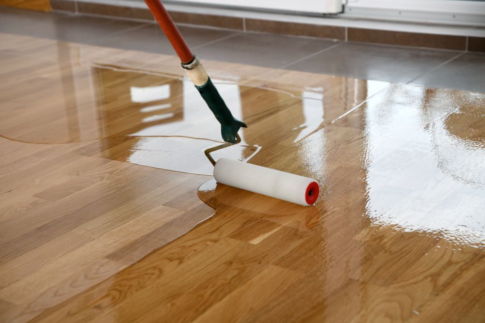 A Person Applies a Clear Sealant to a Wooden Floor — Waters Abrasive Blasting Services In Mission Beach, QLD