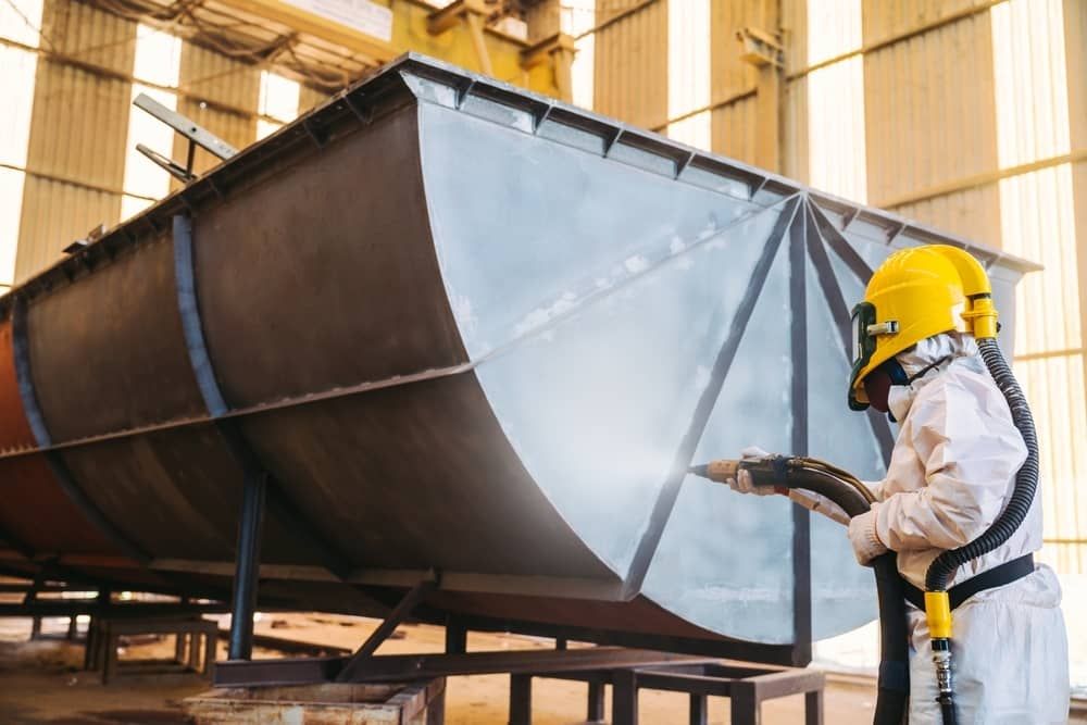 A Man is Sandblasting a Large Piece of Metal in a Factory — Waters Abrasive Blasting Services In Shaw, QLD