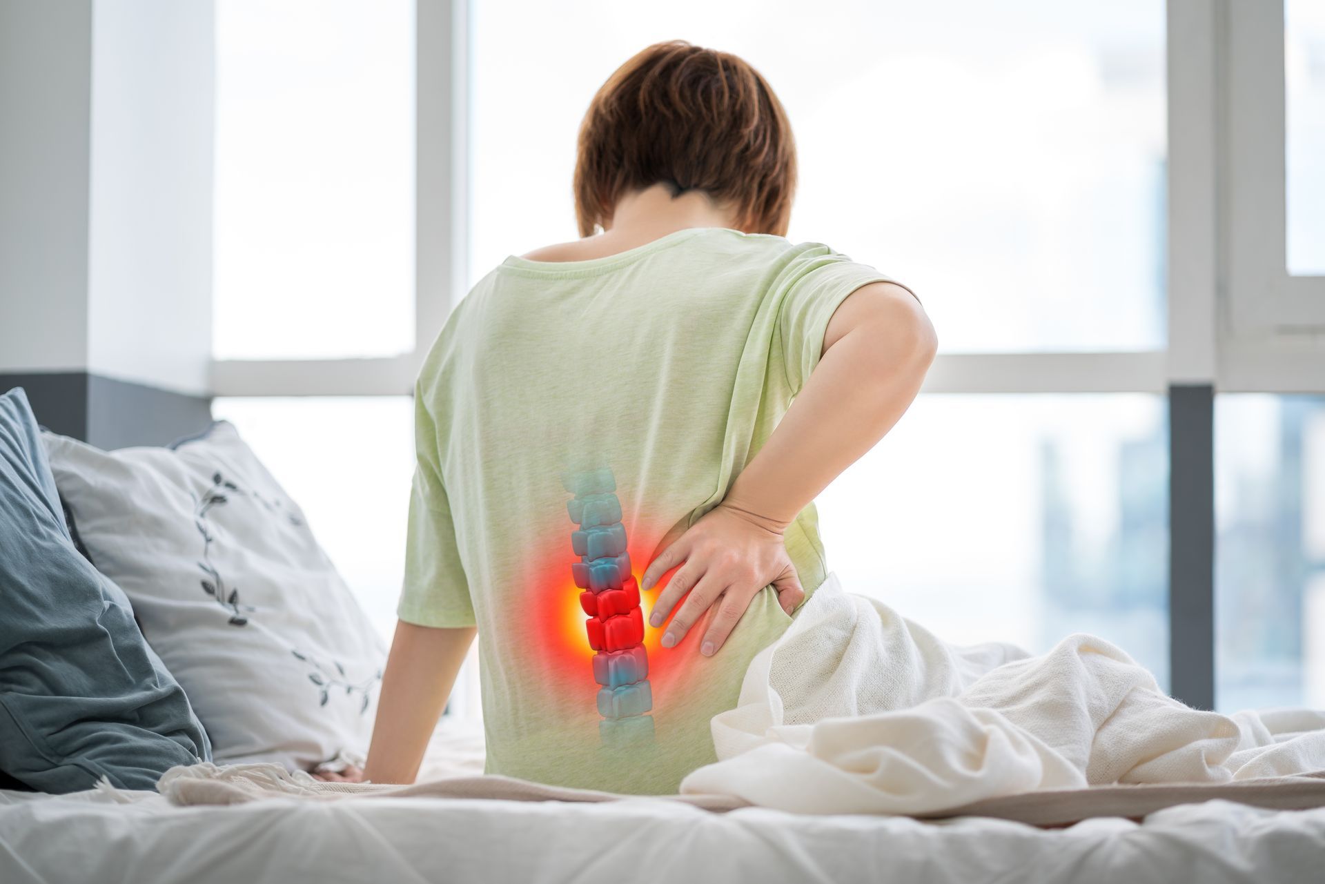 A woman is sitting on a bed with back pain.