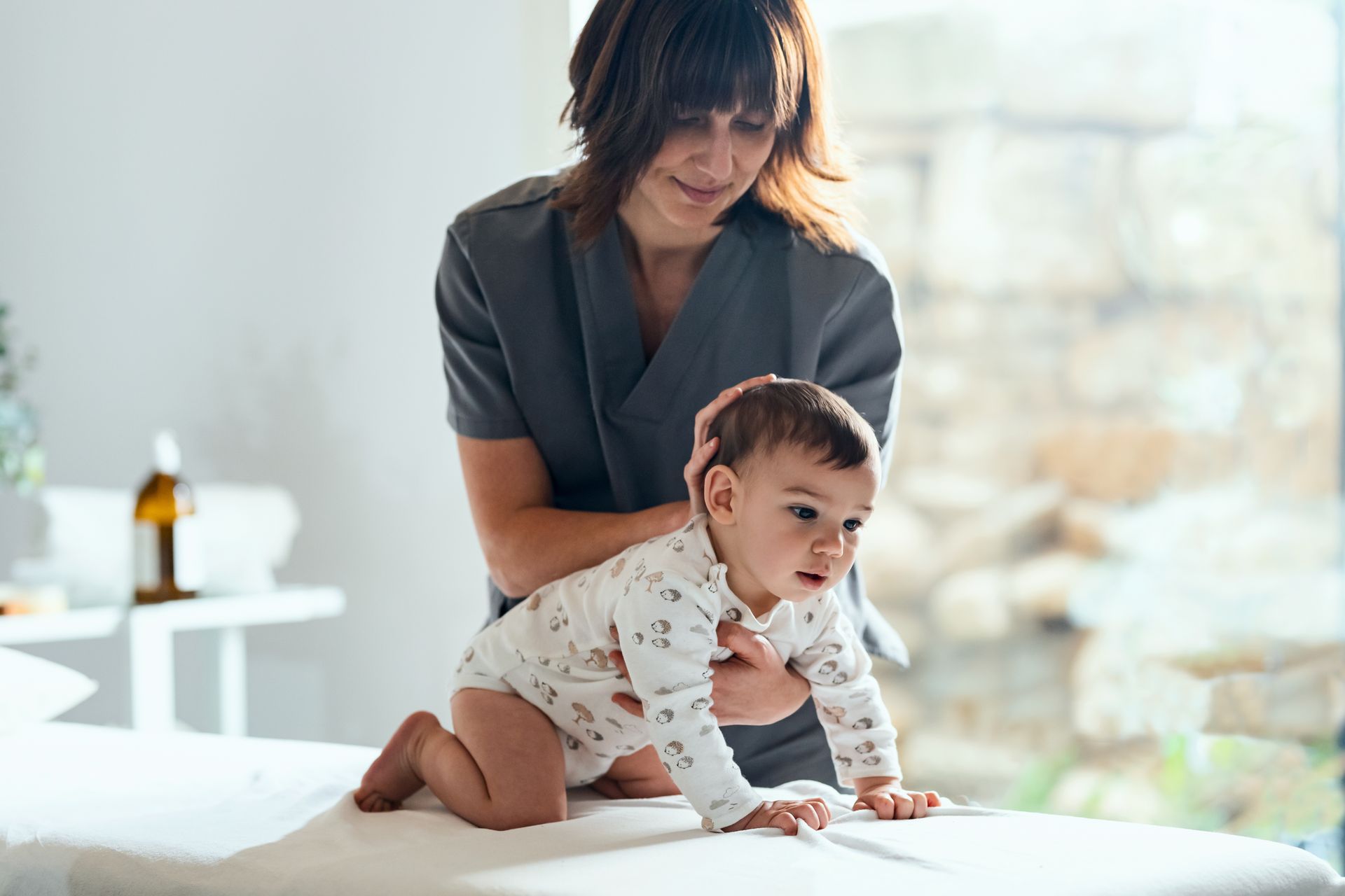 A woman is holding a baby who is crawling on a table.