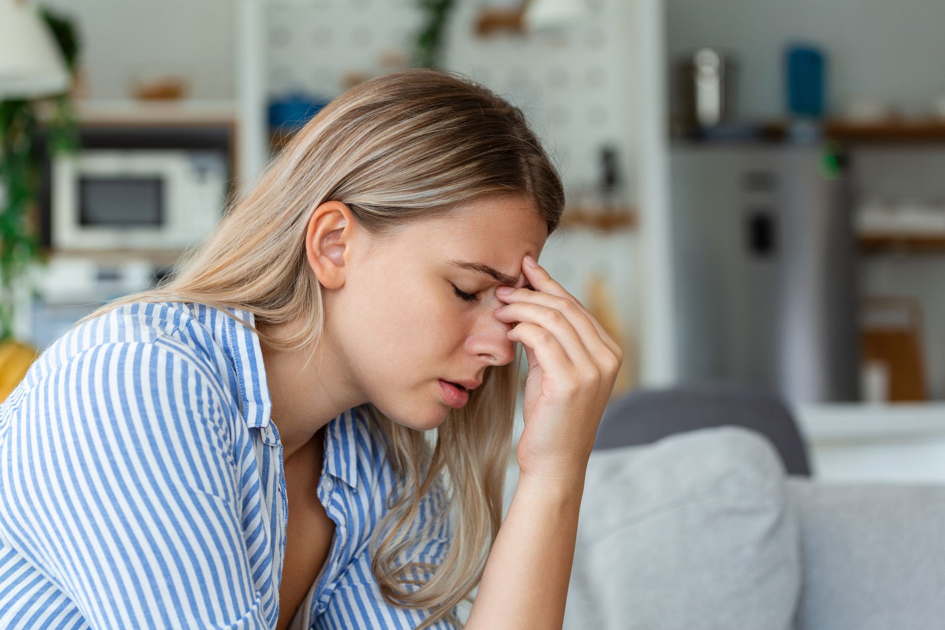 A woman is sitting on a couch with her head in her hands.
