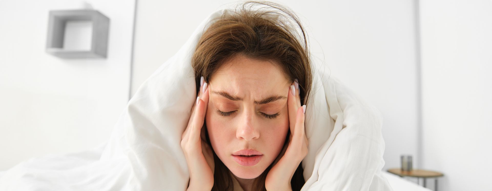 A woman is laying in bed with her head in her hands.