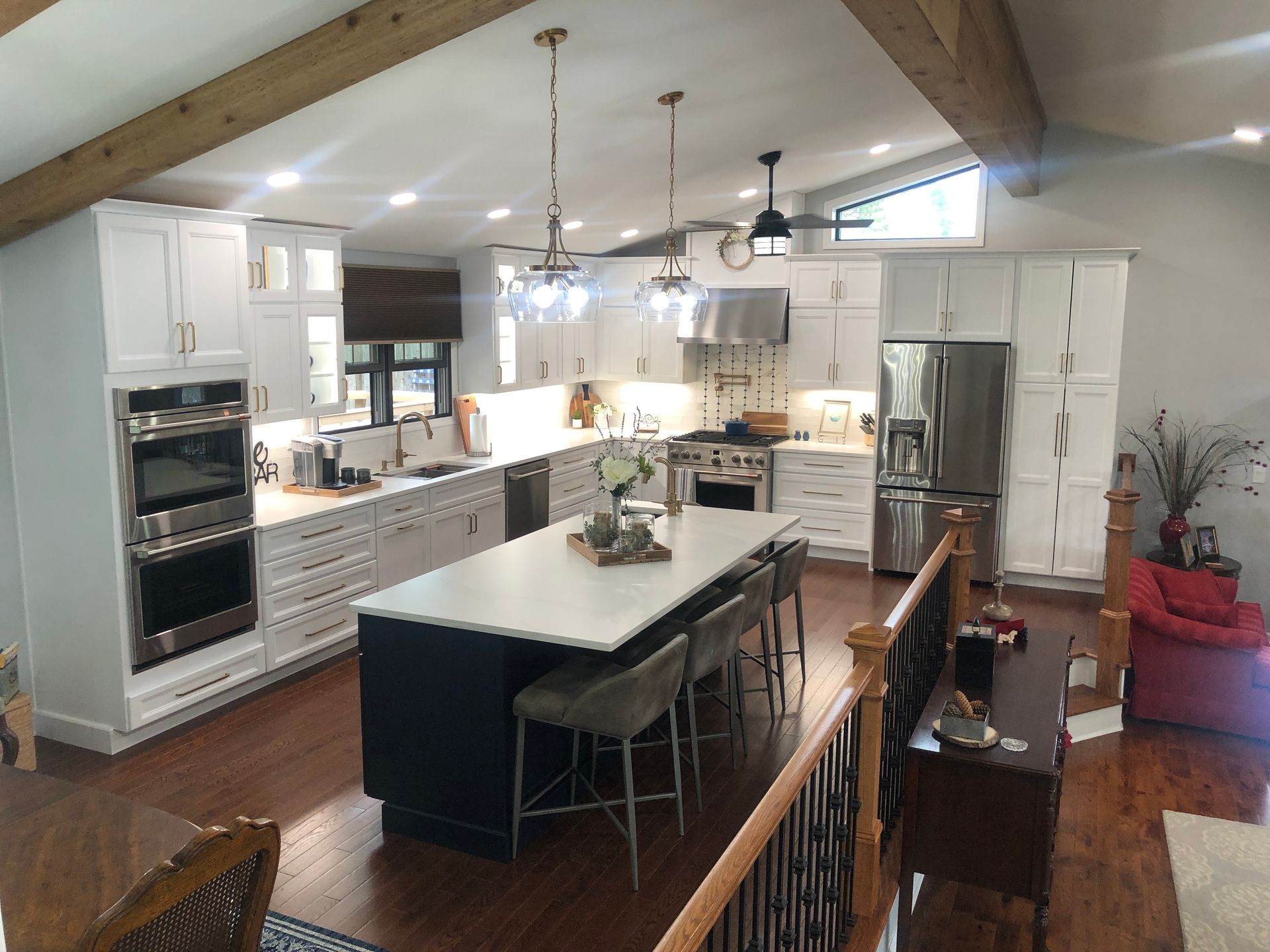 Spacious white kitchen with dark blue island, stainless steel appliances, wood beams, and natural light.