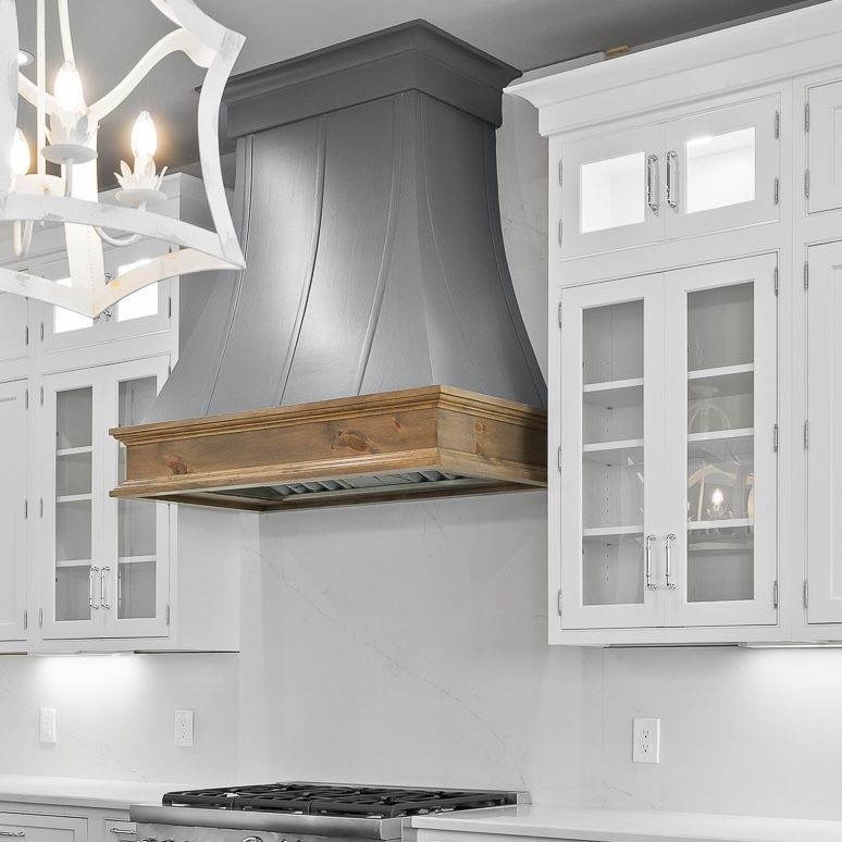 Modern kitchen with white cabinets, gray range hood, and wood-topped vent above a stovetop