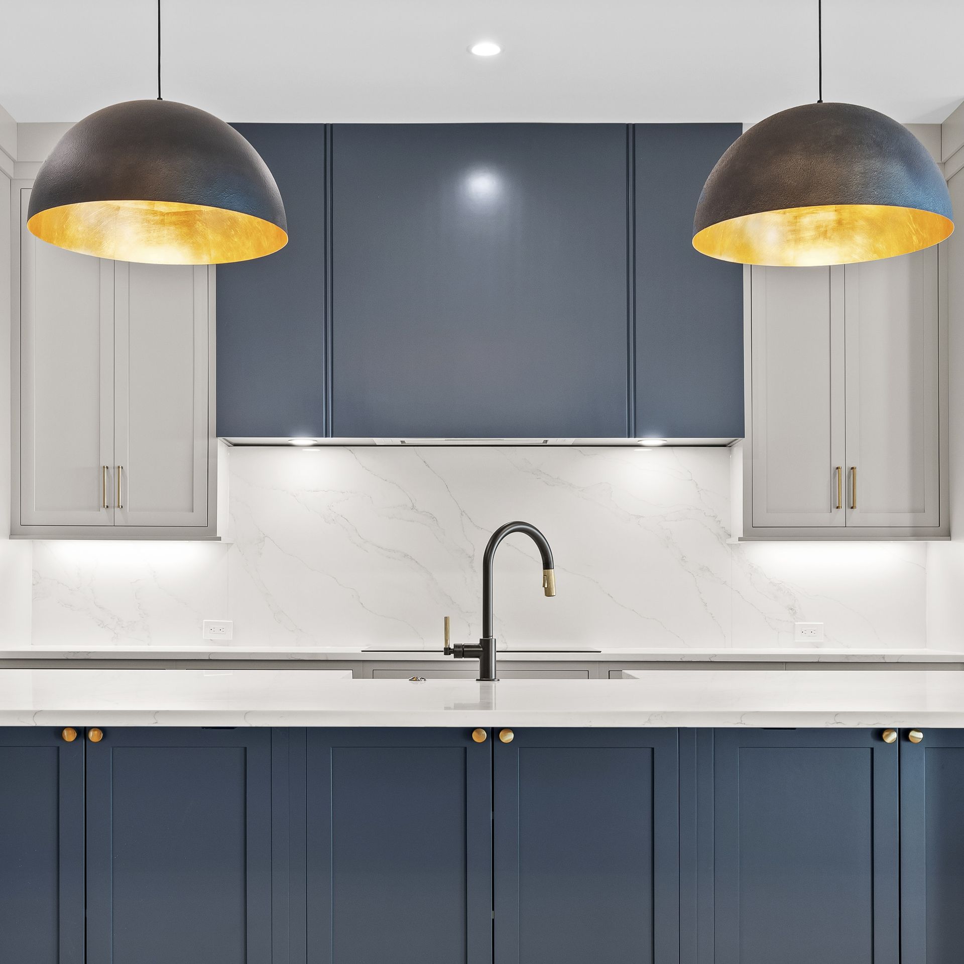 Modern kitchen with navy and white cabinets, marble backsplash, black sink, and two pendant lights