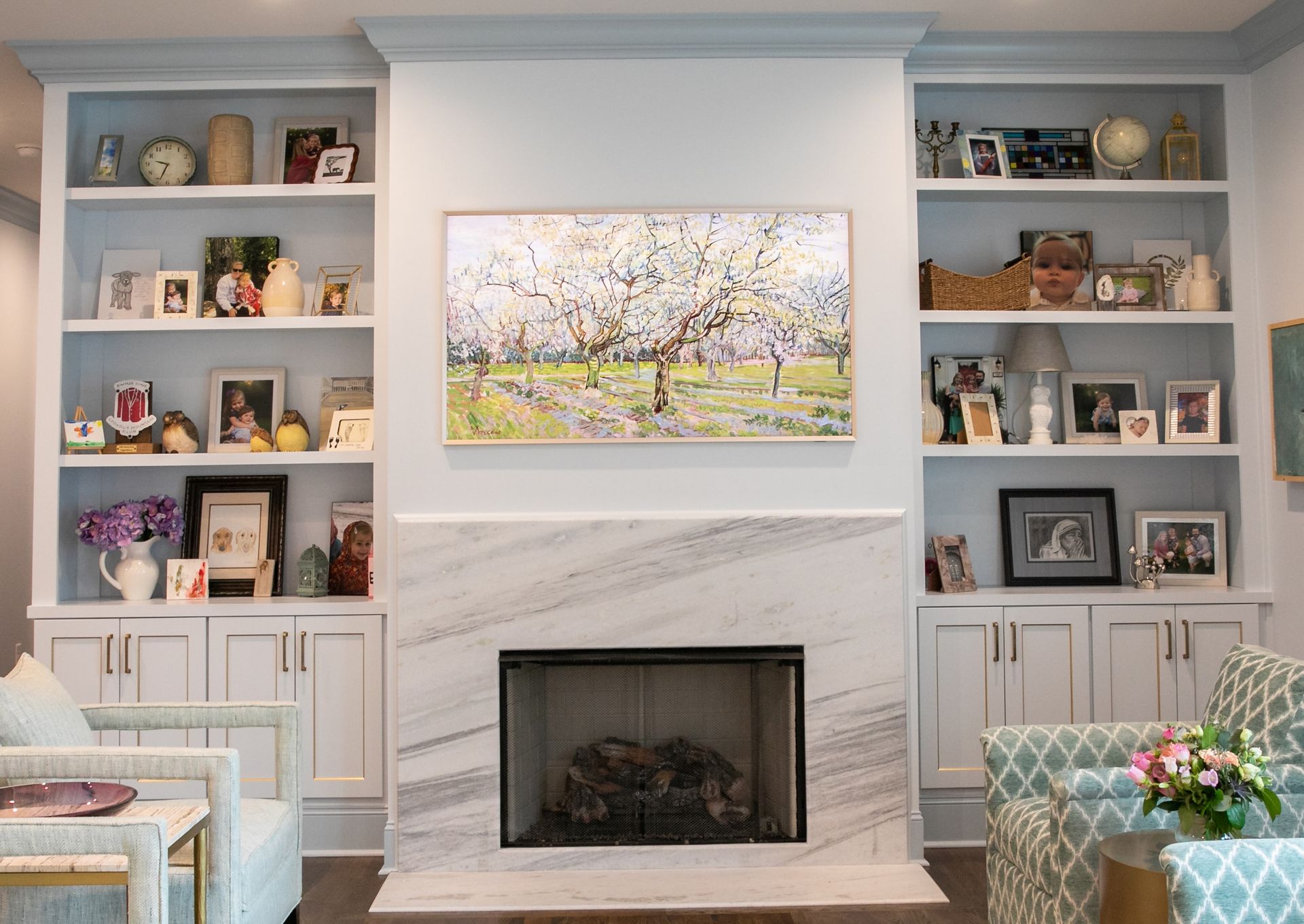 Built-in bookshelves flank a fireplace with a large painting centered above it. Neutral colors dominate the living space.