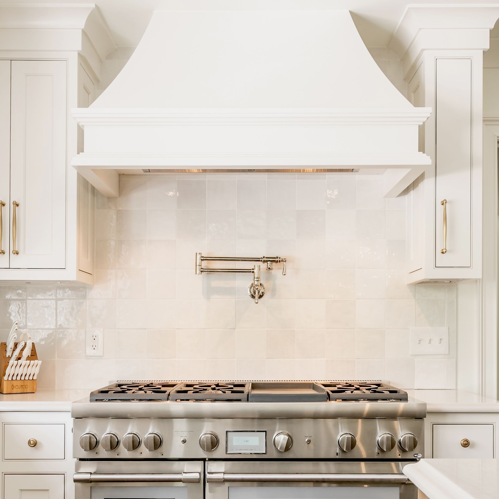 Bright white kitchen with a stainless steel range and hood beneath tiled backsplash and cabinets