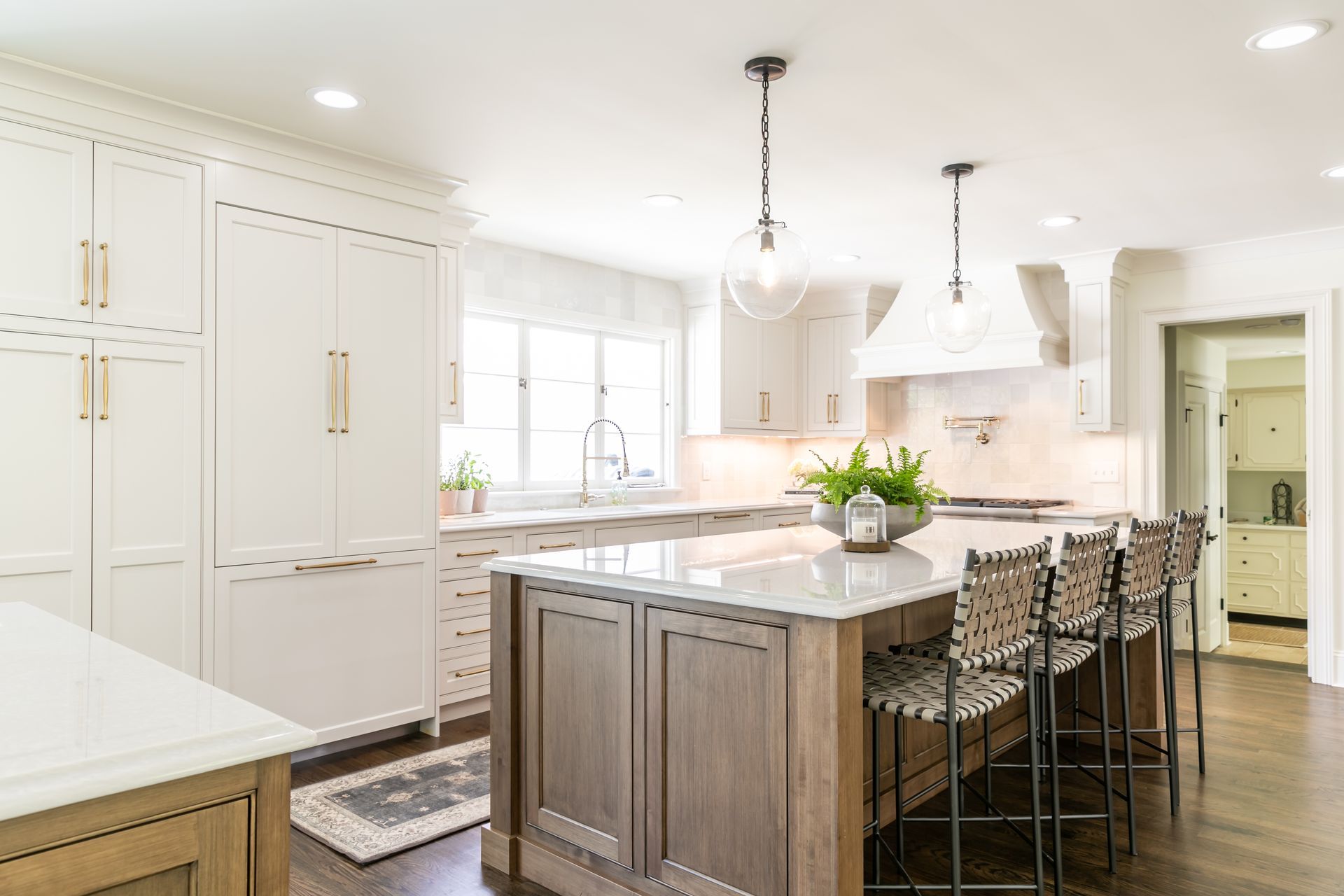 Elegant white and wood-toned kitchen with a large island, bar stools, and a light-filled space.