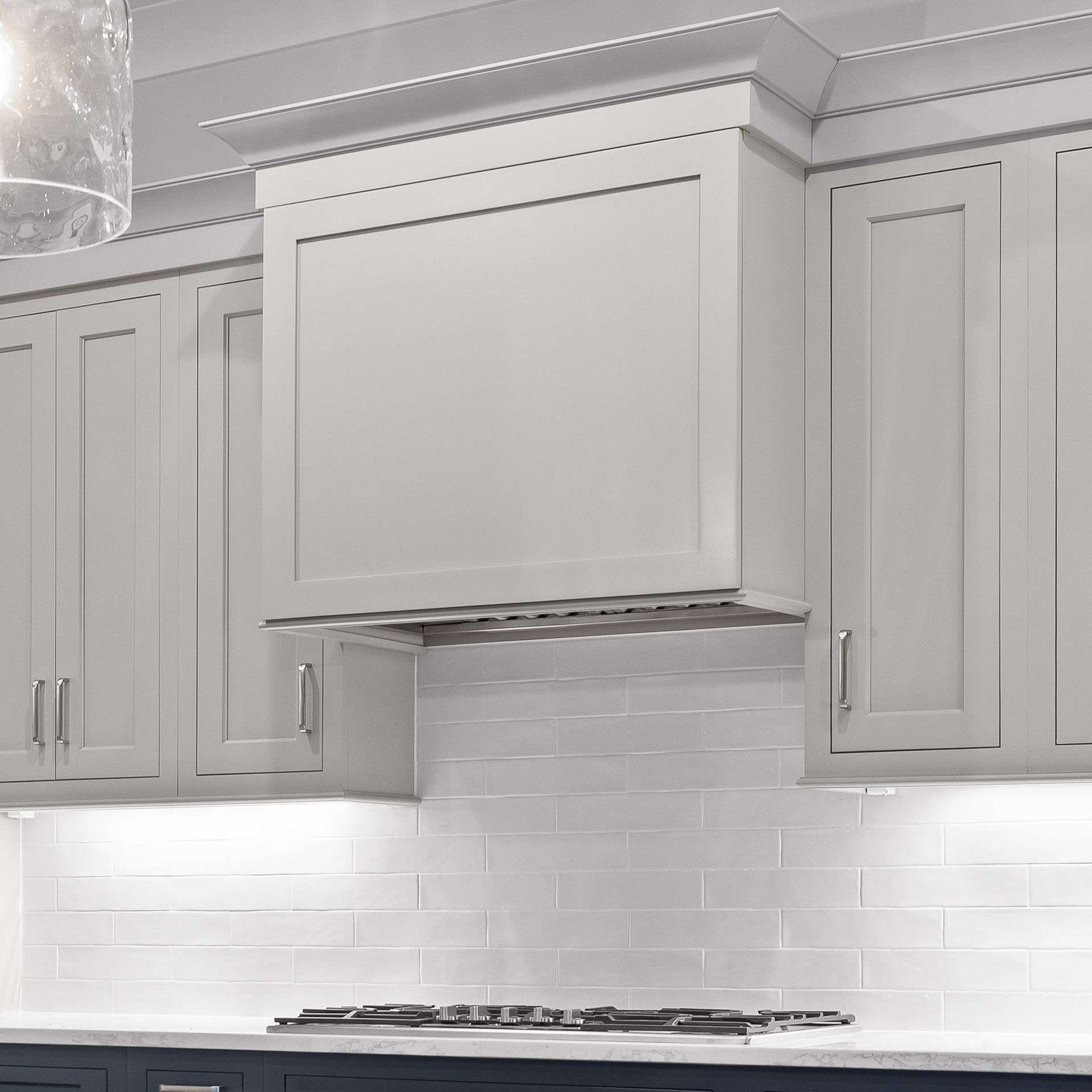 Modern white kitchen with cabinets, subway tile backsplash, and a central range hood above a cooktop
