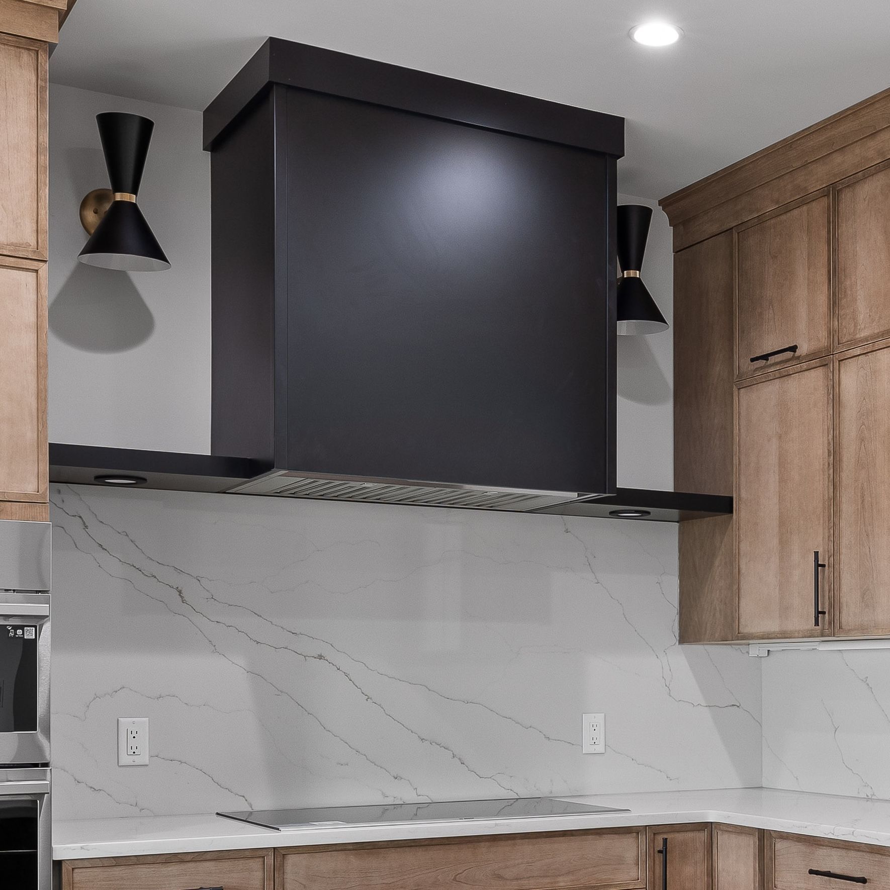 Modern kitchen with black range hood, white marble backsplash, and light wood cabinets