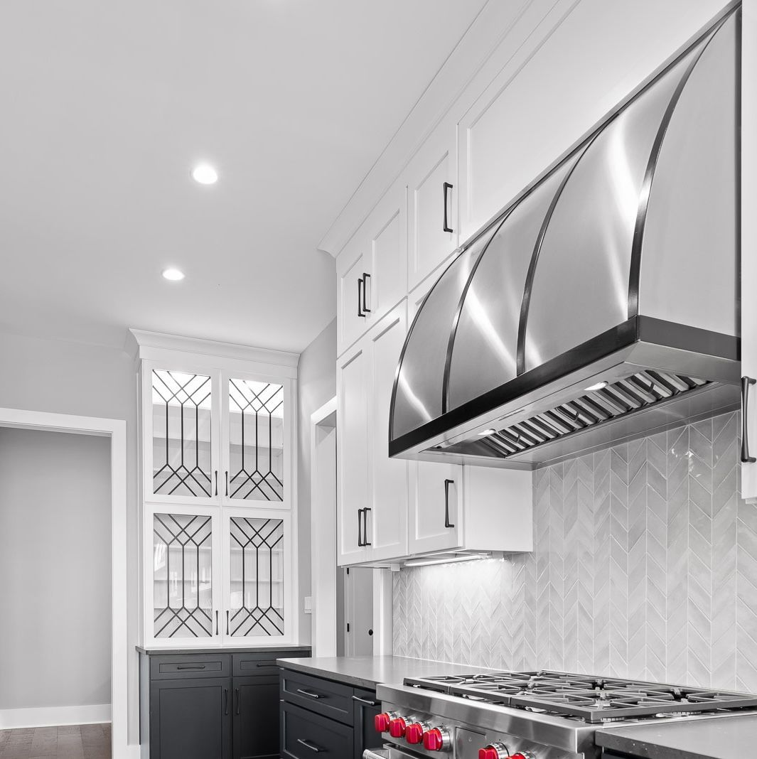Modern white kitchen with stainless steel range hood, gas stove, and patterned backsplash