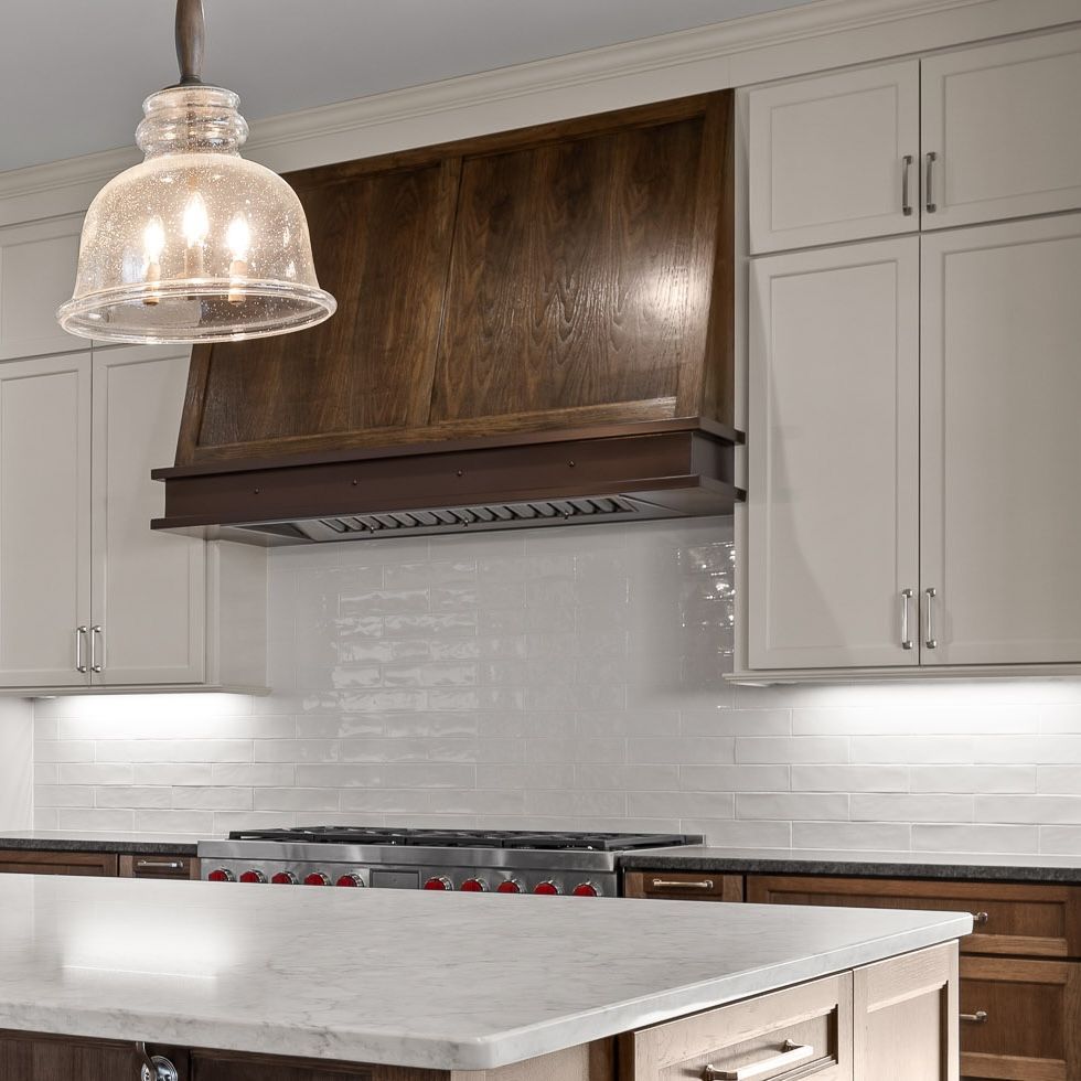 Modern kitchen with white cabinets, dark wood range hood, and light stone island countertop