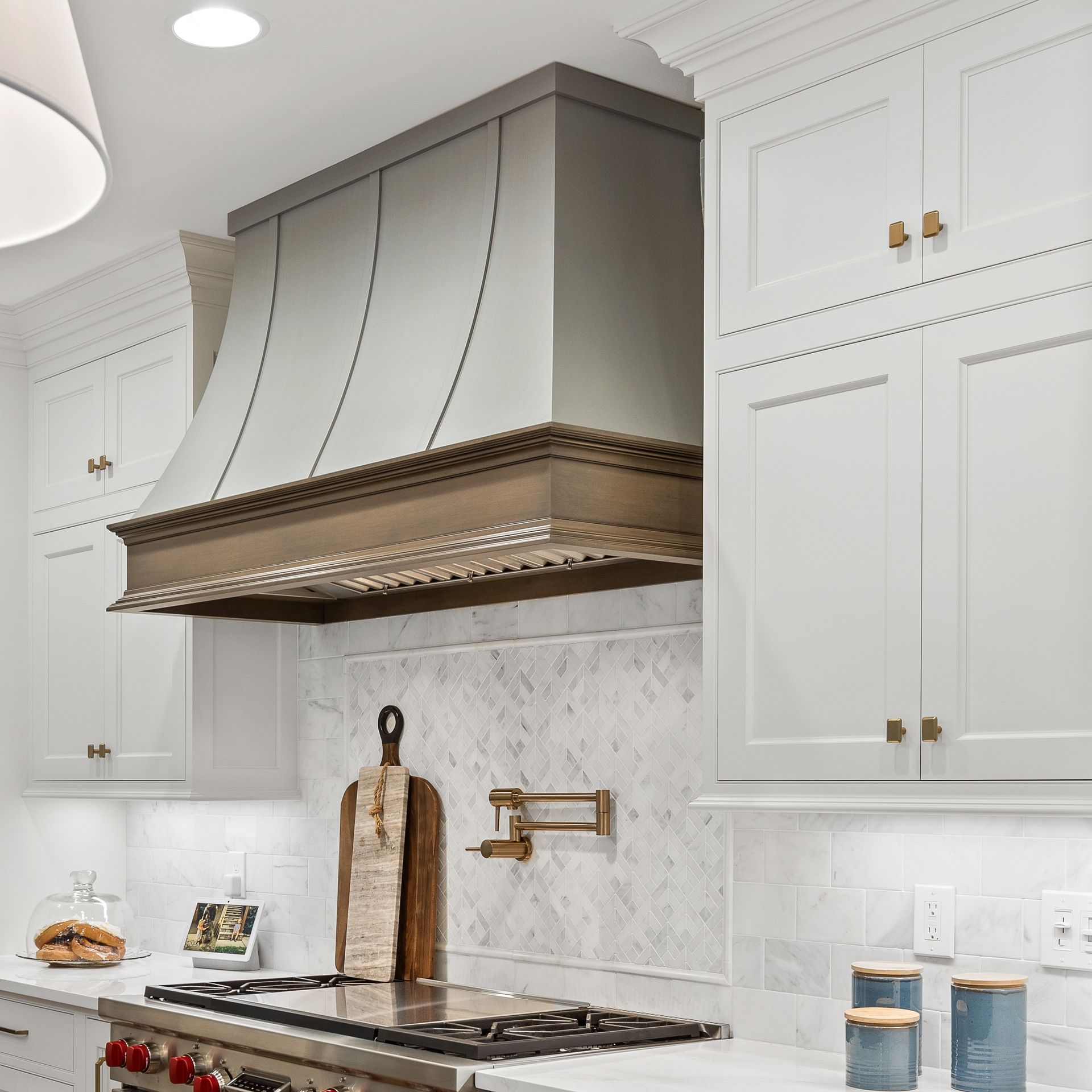 Modern white kitchen with gray range hood, marble backsplash, and brass accents
