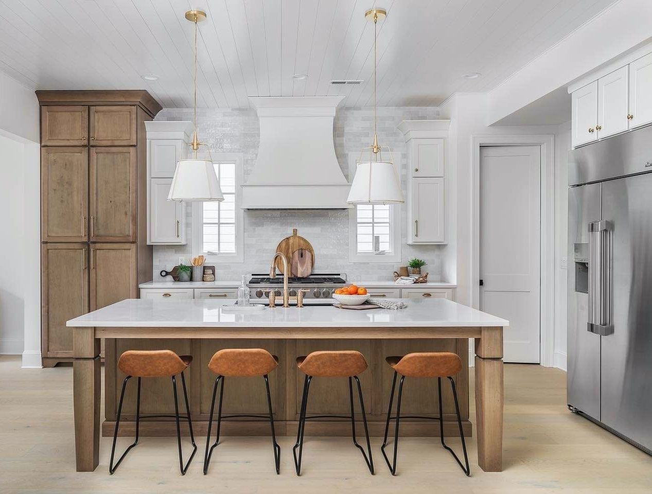 Kitchen with island, light wood cabinets, stainless steel refrigerator, and brown bar stools.