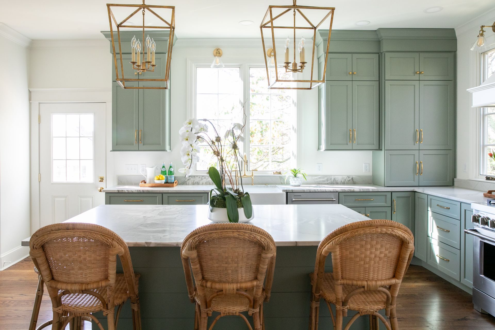 Green kitchen with wicker bar stools and gold light fixtures.