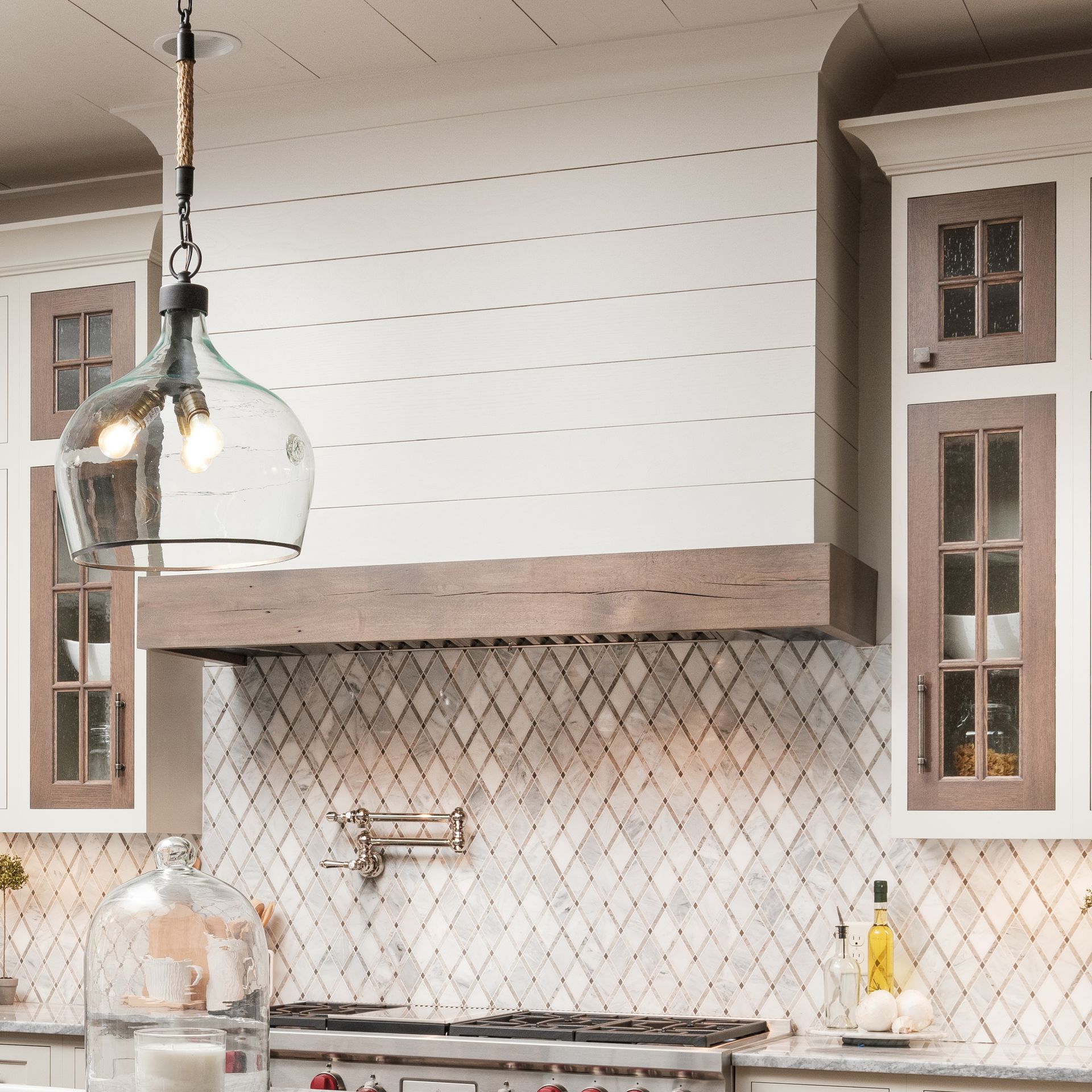 Bright kitchen with white shiplap walls, tiled backsplash, wood range hood, and hanging glass pendant lights