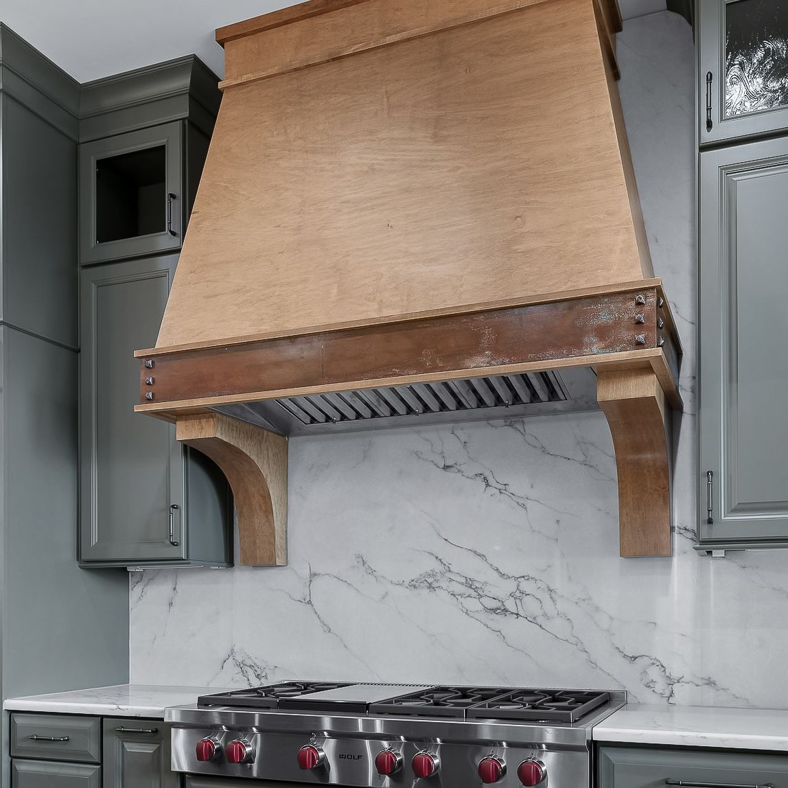 Modern kitchen with a large wooden range hood above a stainless steel stove and marble backsplash