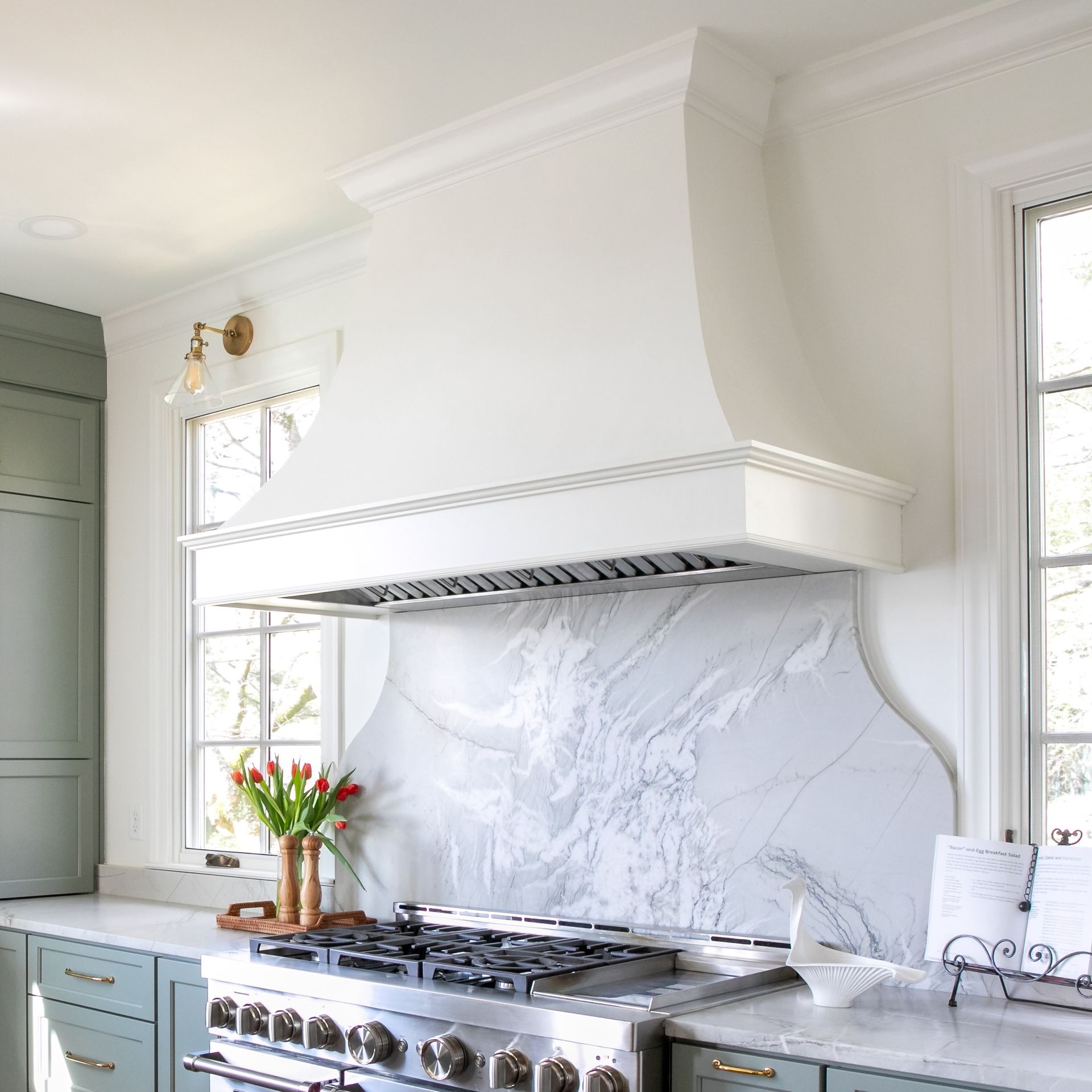 Bright white kitchen with blue cabinets, marble backsplash, and stainless steel range hood