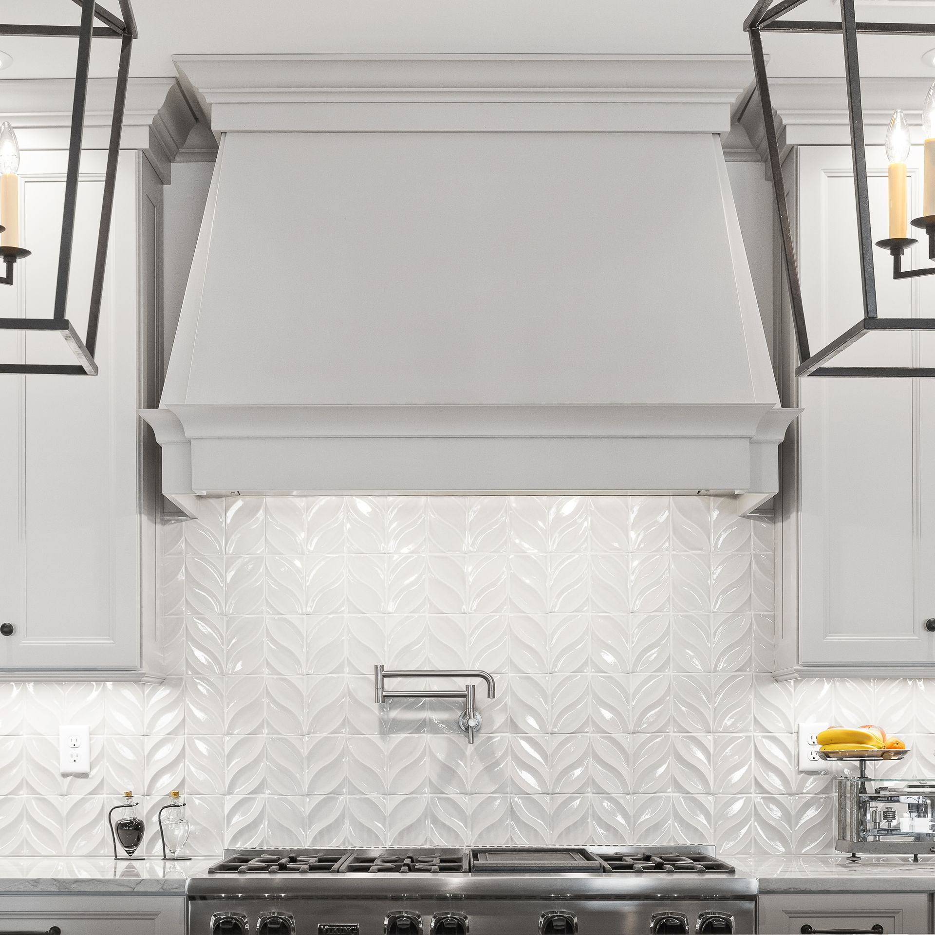Modern white kitchen with a chevron tile backsplash, stainless stove, and large white range hood