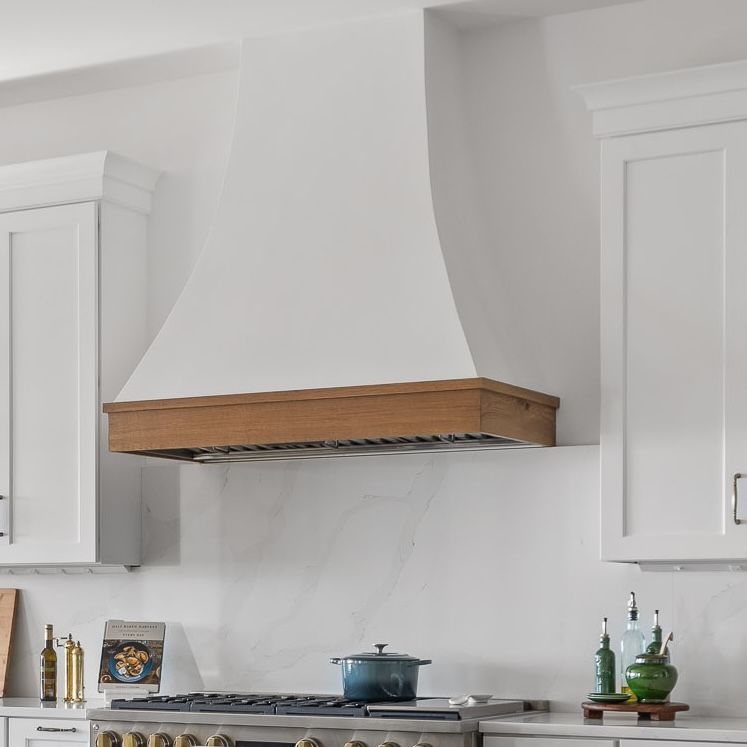 Modern white kitchen with a central range hood, wooden trim, and stove beneath marble-patterned backsplash