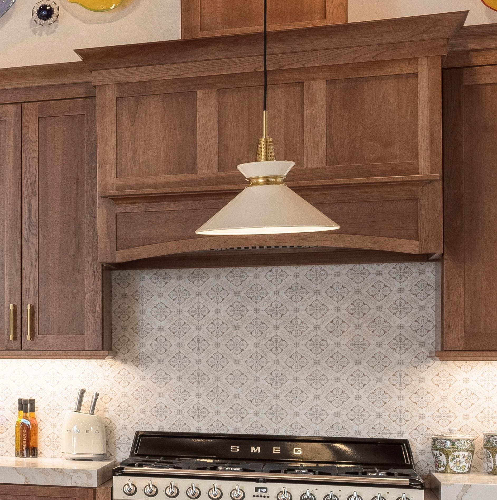 Modern kitchen with wood cabinets, white pendant light, and patterned backsplash above the stove