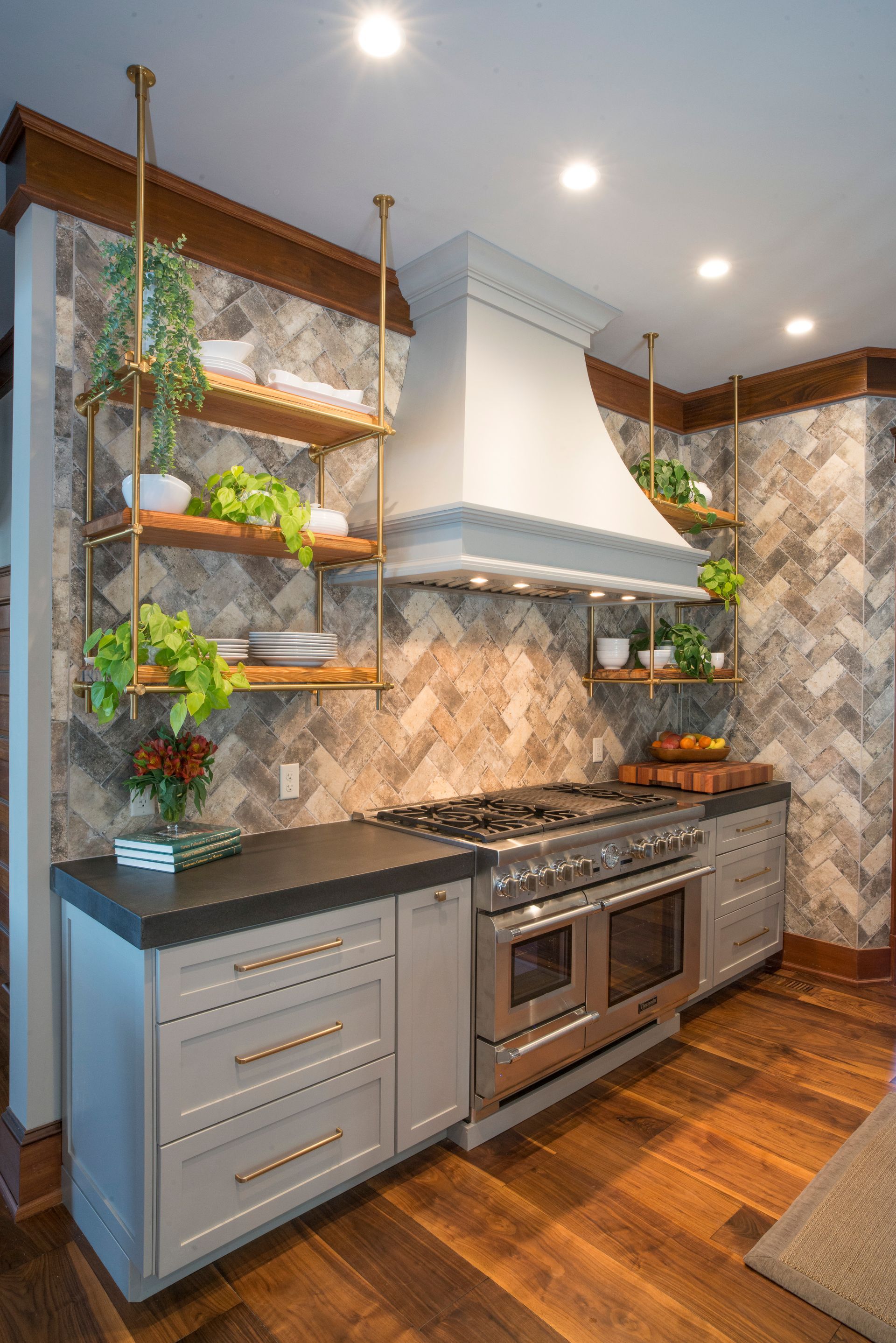 Gray kitchen with a range, range hood, open shelving with plants, and wood floors.