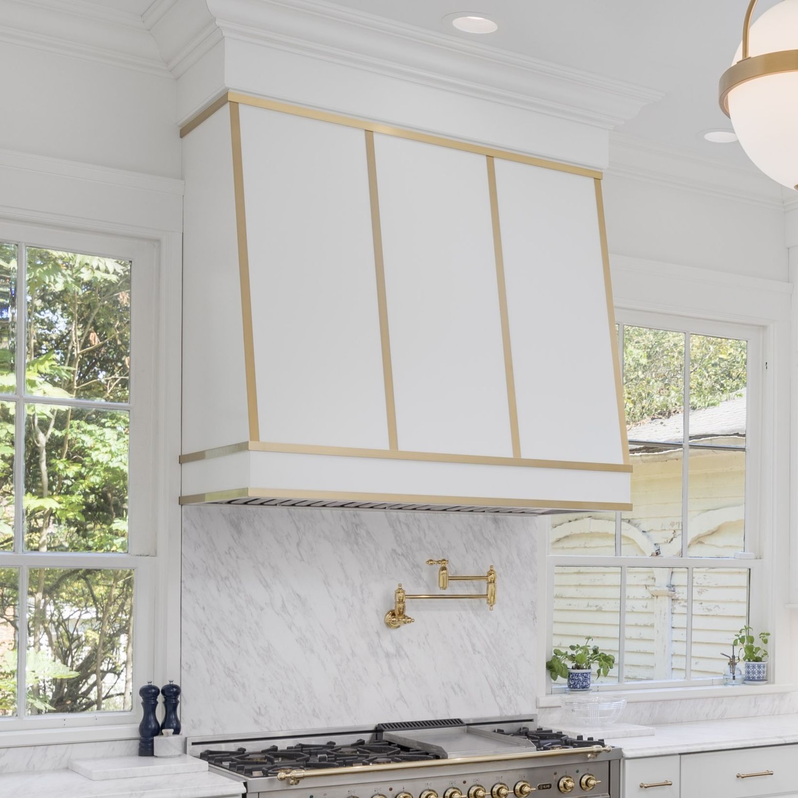 White kitchen with gold-trimmed cabinets, marble backsplash, and a gas range beneath a window