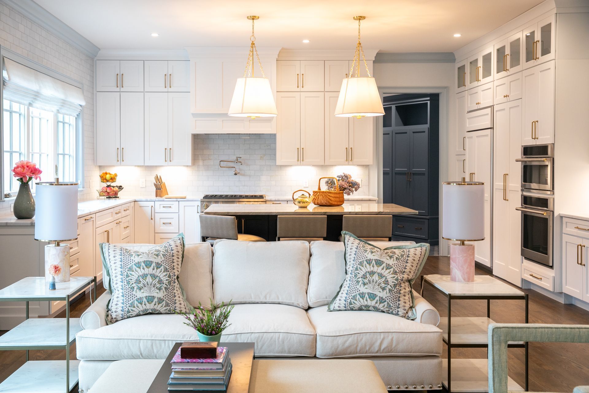 Bright kitchen and living room area with white cabinets, a light-colored sofa, and two hanging pendant lights.