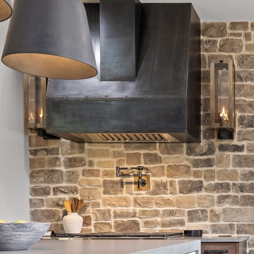 Modern kitchen with stone backsplash, black range hood, and pendant light over a countertop