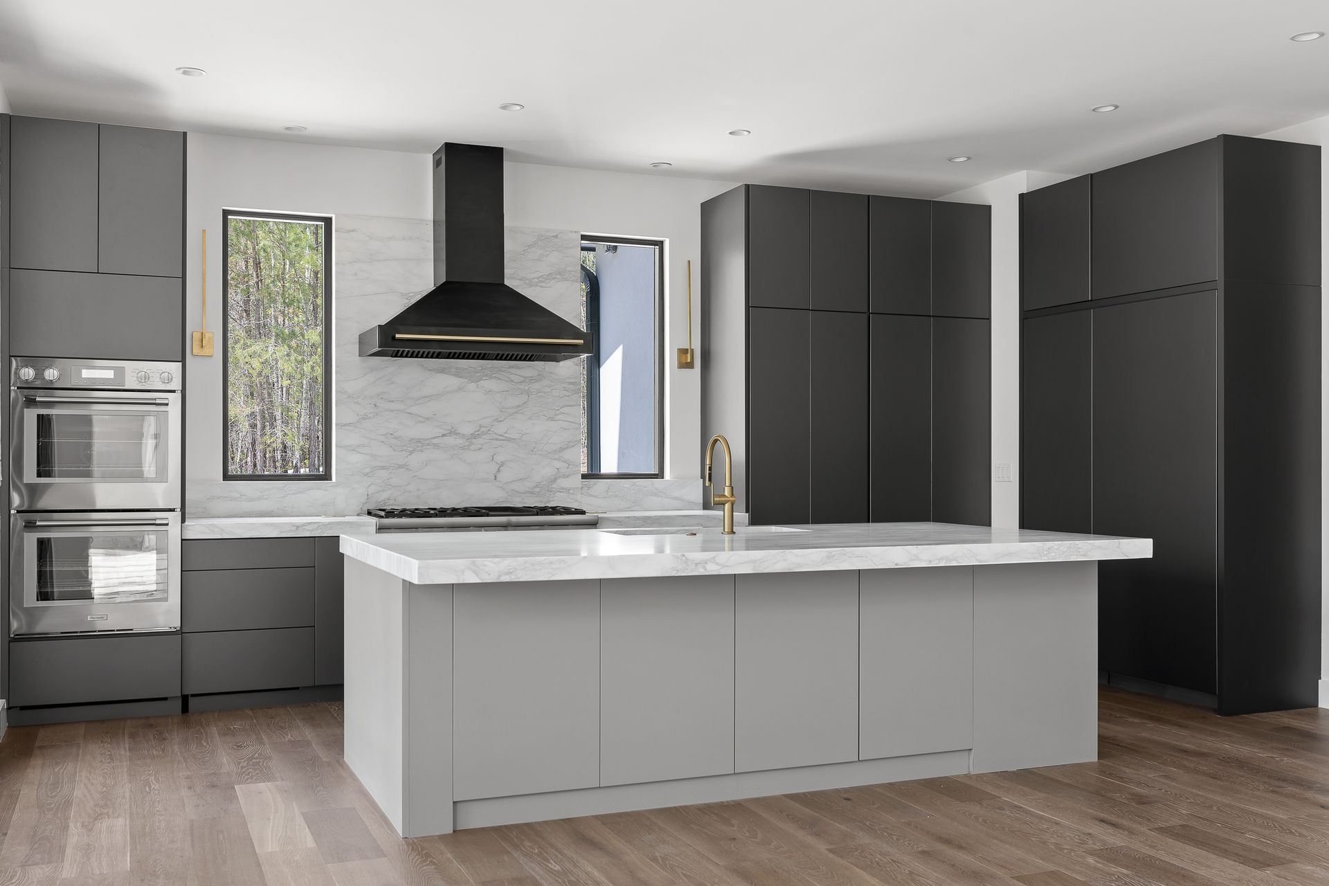 Modern kitchen with gray cabinets, white countertops, stainless steel appliances, and a black range hood.