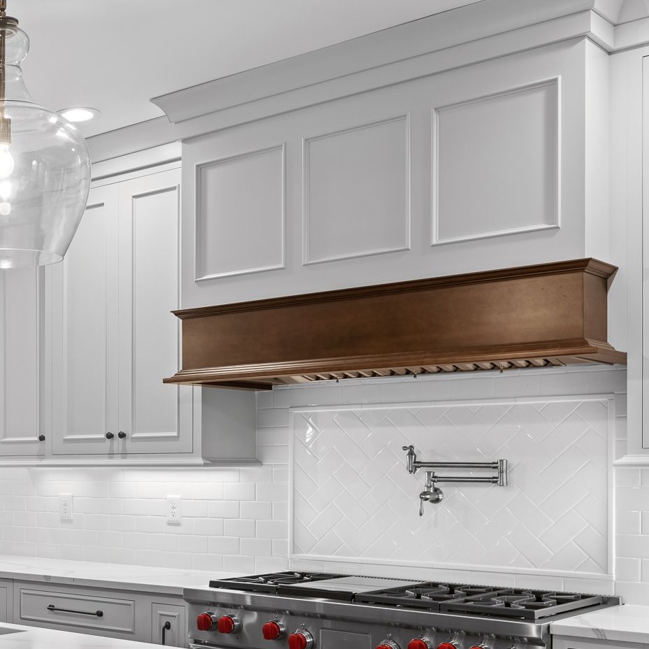 White kitchen with gray cabinets, wood range hood, and a stainless gas cooktop.