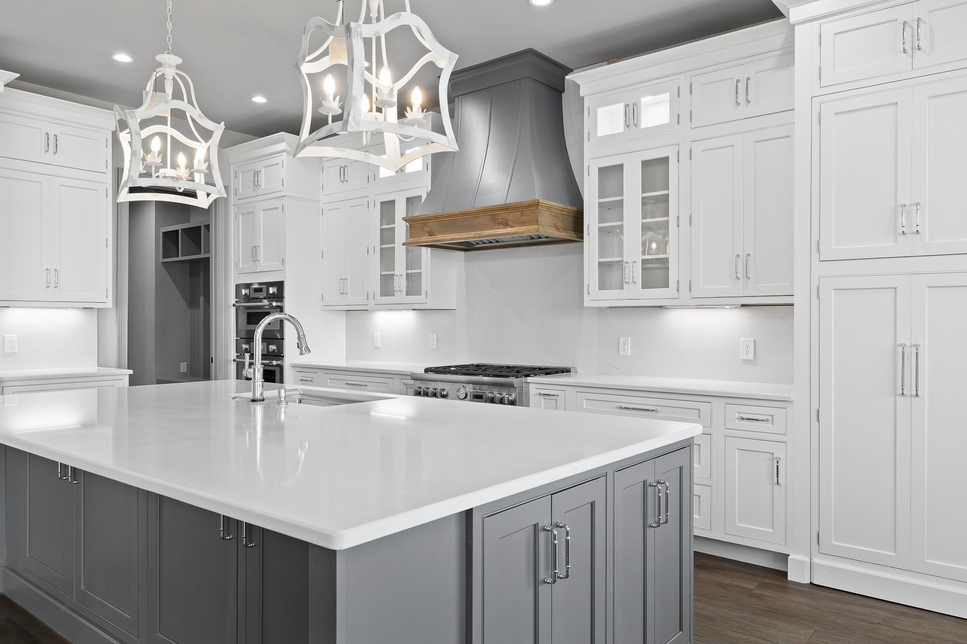 Modern white kitchen with gray island, white countertops, and decorative lighting.