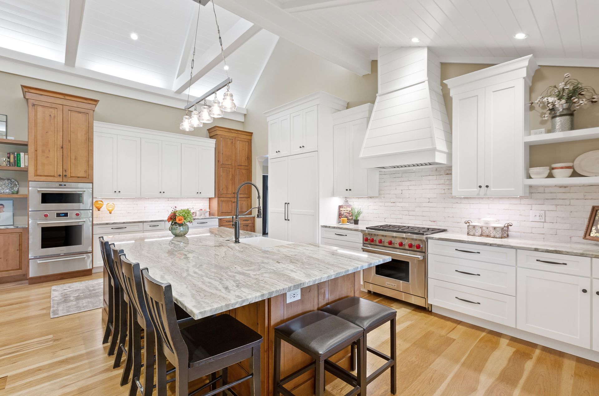 Luxurious kitchen: white cabinets, island with granite countertop, wooden floor, and stainless steel appliances.